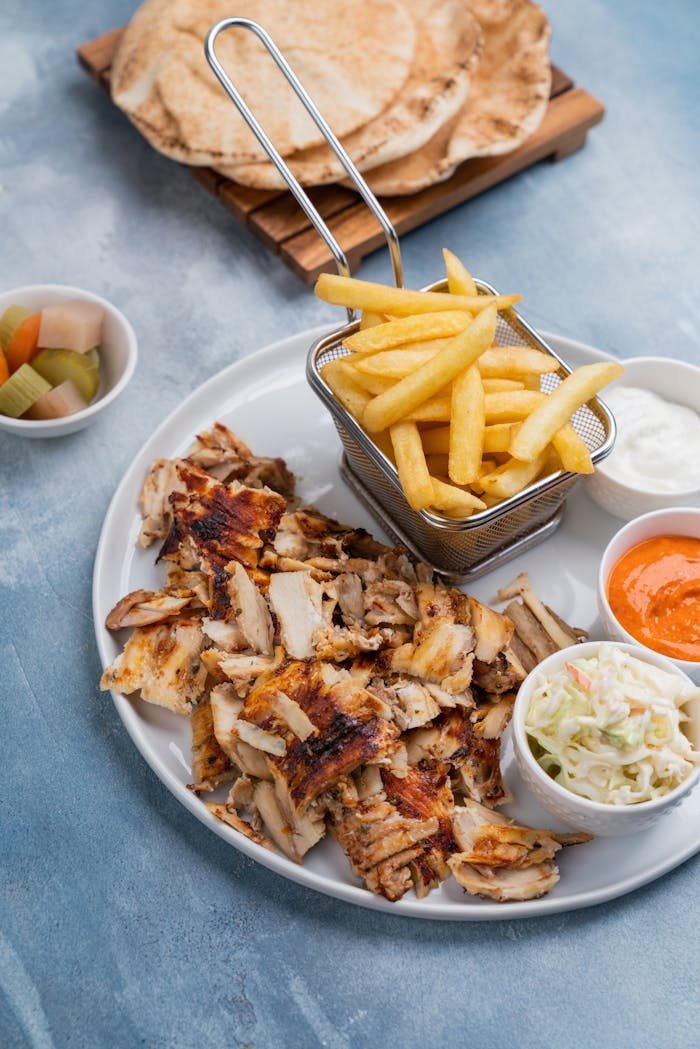 Top view of a Middle Eastern meal with grilled chicken, fries, and dips, perfect for lunch or dinner.
